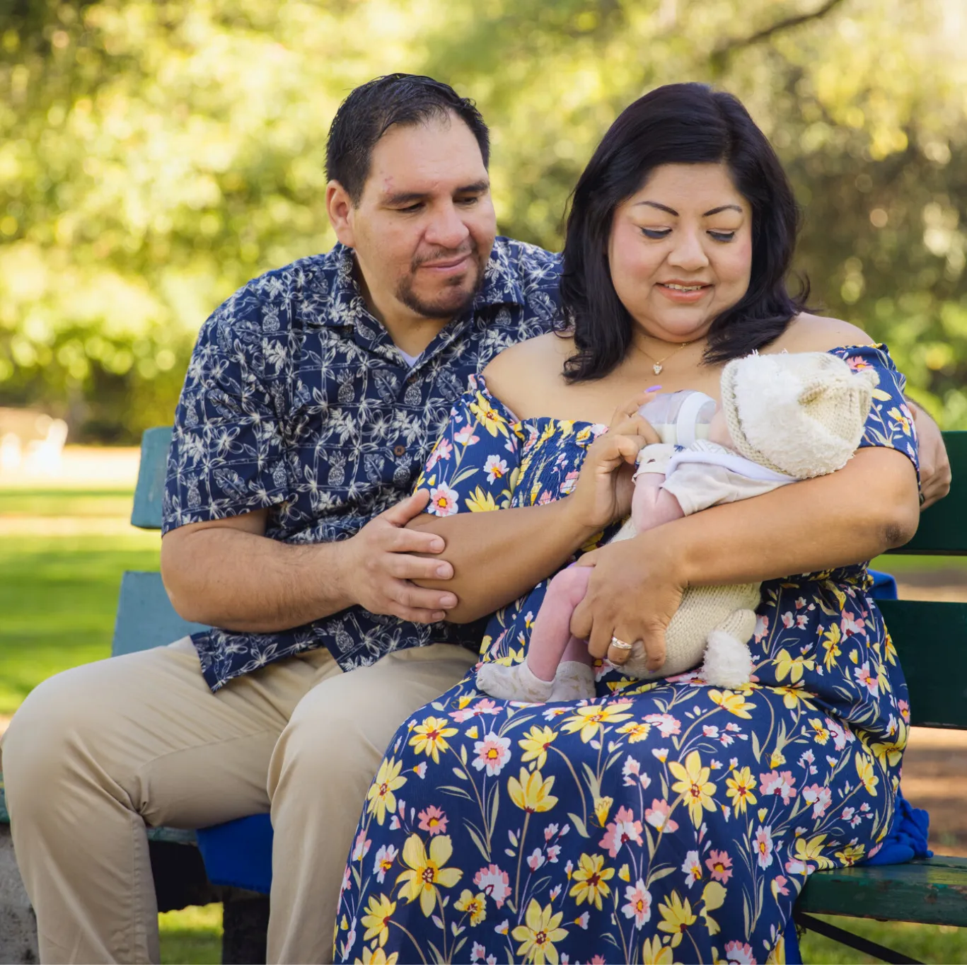 A dad and woman sitting on a park bench holding newborn
