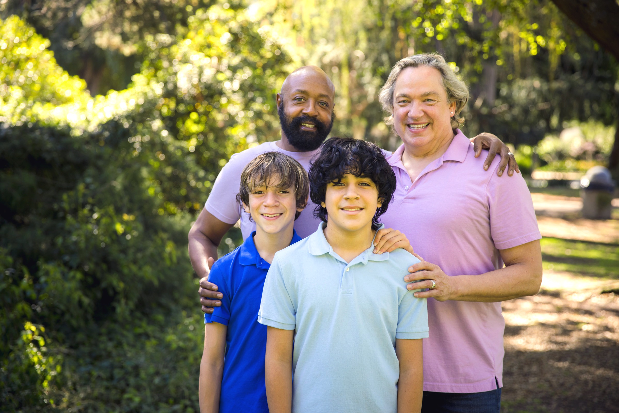 Two dads wearing purple tops standing behind their two teenage sons