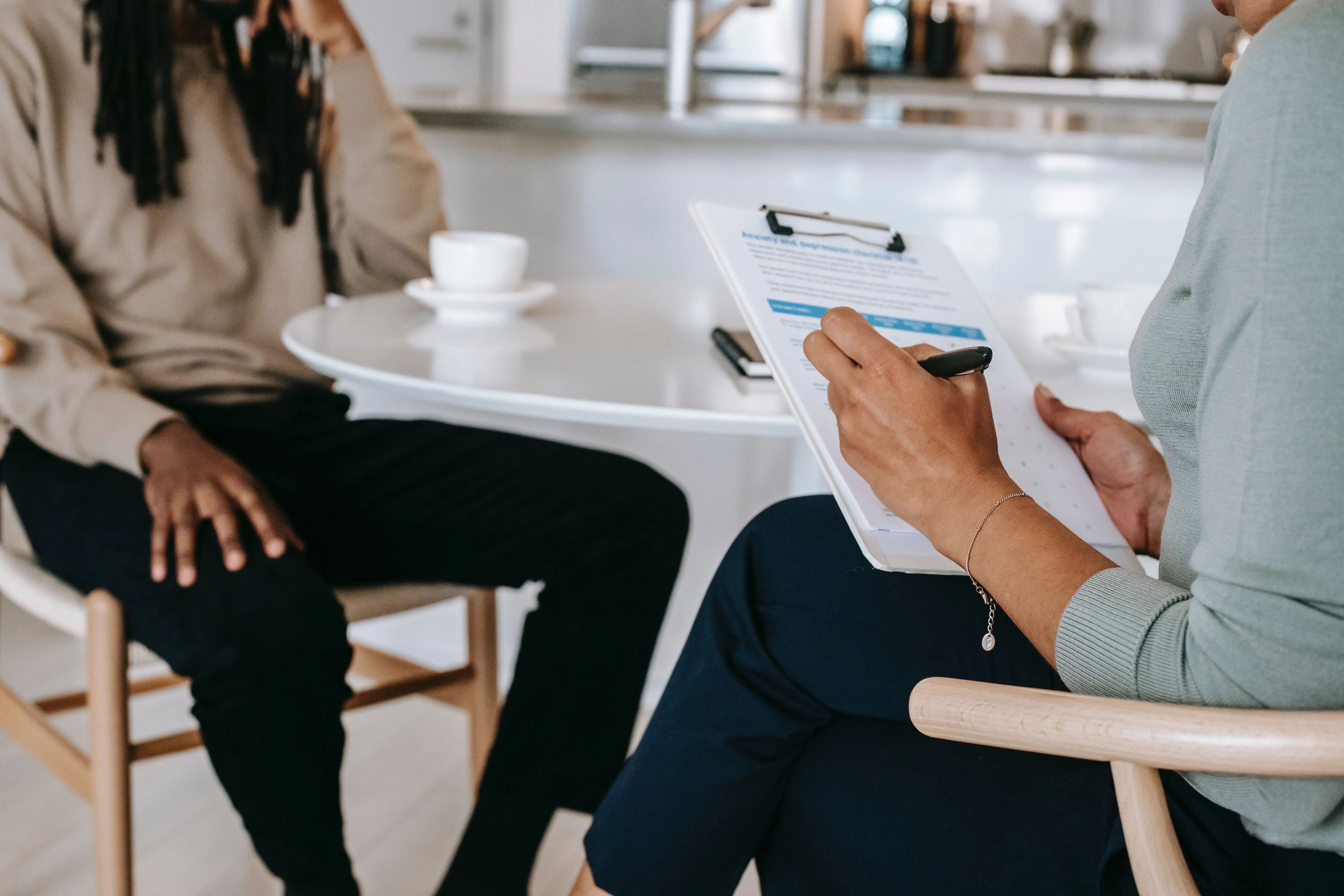 Two people sitting at a coffee table with one person having a clipboard completing an evaluation of the other person